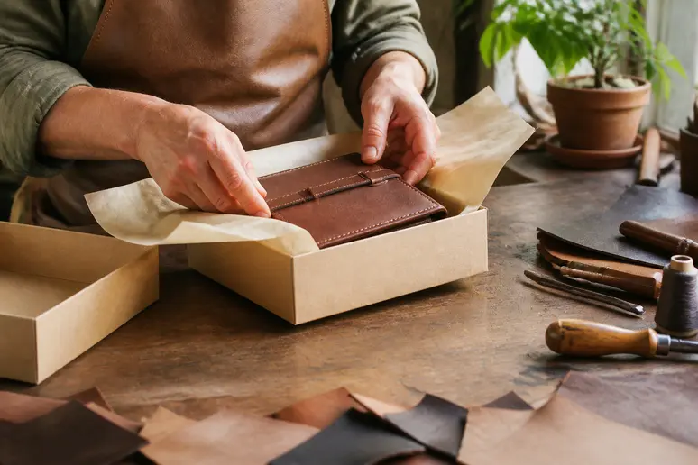 Artisan packaging a handmade leather craft in a workshop during big cartel vs etsy comparison