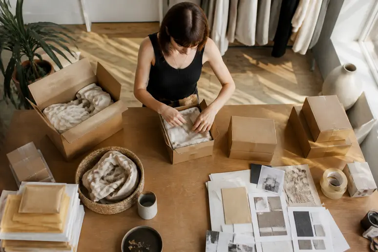 Independent maker organizing product packaging and shipping boxes in a studio