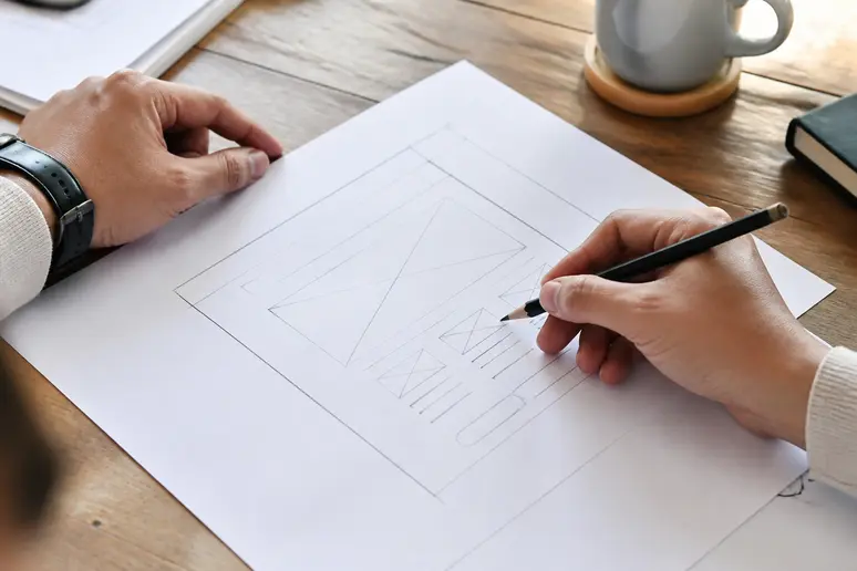 Designer sketching SEO landing page wireframe and simplified conversion forms on paper