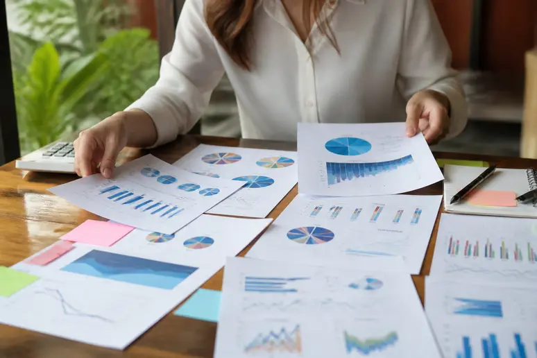 Digital strategist organizing detailed monthly performance reports and analytics data